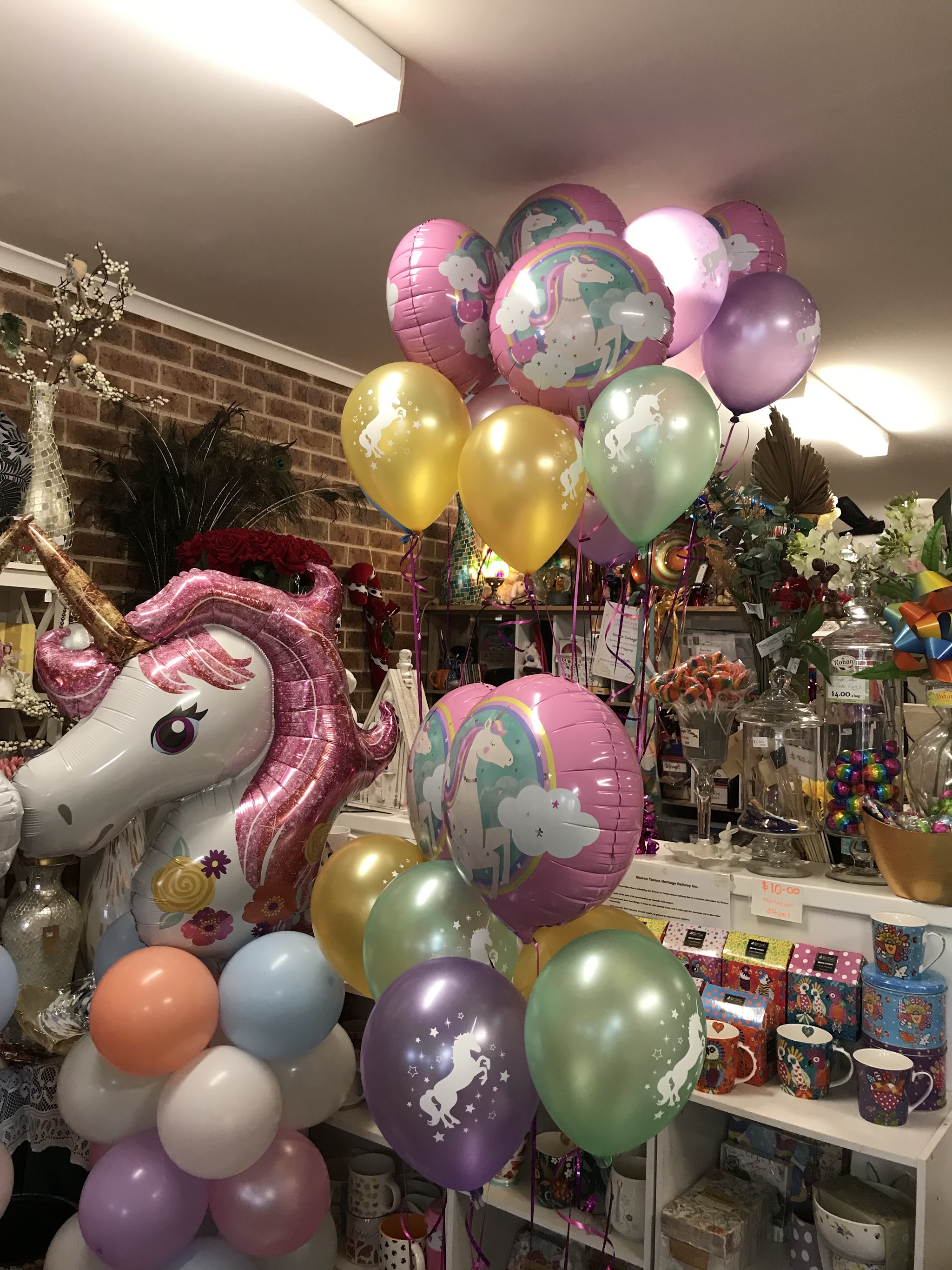 A unicorn balloon display with pastel balloons, mugs and gift boxes on the shelves