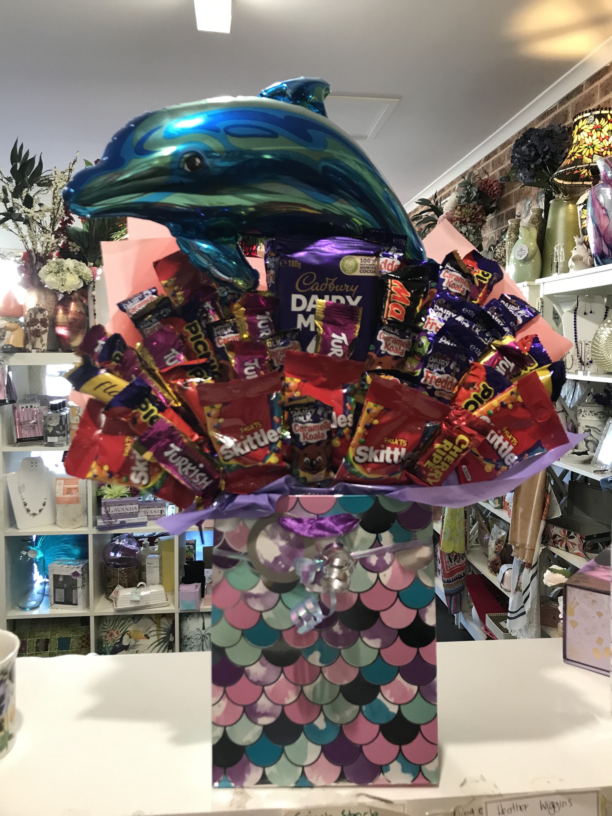 A chocolate and lolly bouquet in a mermaid scale gift bag, topped with a blue dolphin balloon