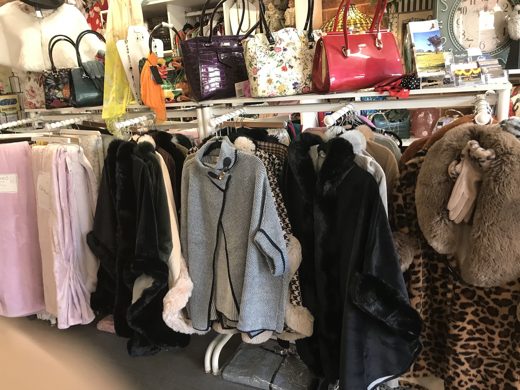 A rack of faux fur wraps, ponchos and scarves with handbags lined up on the shelf above